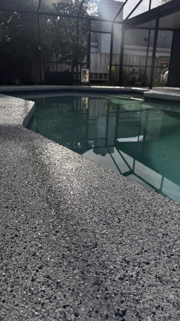 Gray flake epoxy pool deck coating around a screened-in pool